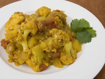 Картофель с цветной капустой и томатами в белой тарелке с кинзой