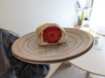 Блинный рулетик в разрезе с клубникой и сливочным кремом на тарелке