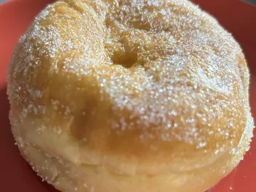 Круглый пончик с дыркой, обвалянный в сахаре, на красной тарелке