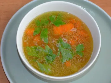 Белая миска с прозрачным бульоном, морковью и петрушкой