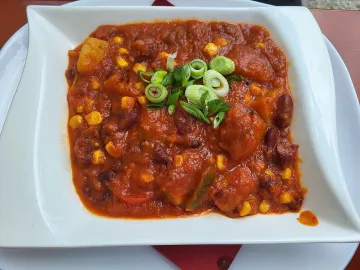 Чили с красной фасолью, кукурузой и зелёным луком в белой тарелке
