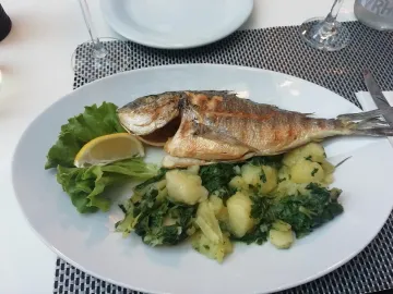 Запечённая рыба с лимоном, картофелем и зеленью на белой тарелке