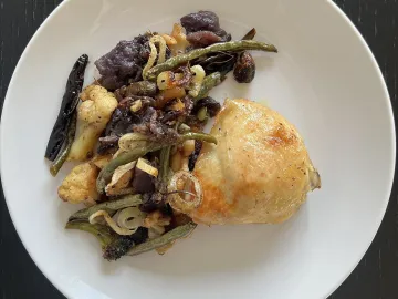 Запечённое куриное бедро с овощами на белой тарелке
