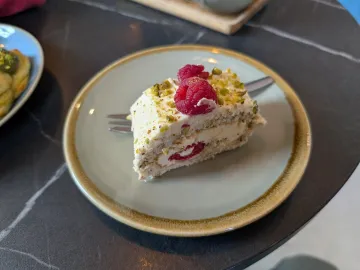 Кусок бисквитного рулета с фисташками, кремом и малиной на тарелке
