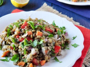 Салат из чечевицы с овощами и зеленью на белой тарелке