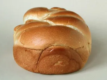 Золотистая булка бриошь с плетёной верхушкой на светлом фоне