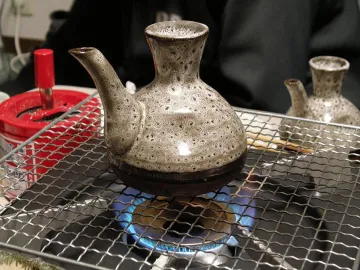 Керамический кувшинчик токкури с саке над газовой горелкой