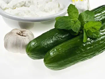 Свежие огурцы, мята и чеснок рядом с миской кисломолочного продукта