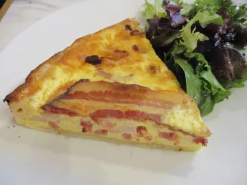 Кусок киша лорен с беконом и салатом на тарелке