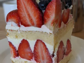 Кусок бисквитного торта с клубникой, сливками и черникой