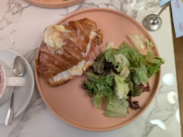 Круассан с беконом, яйцом и расплавленным сыром, рядом зелёный салат
