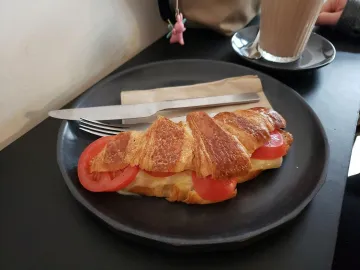 Запечённый круассан с сыром и кружками помидора на тёмной тарелке
