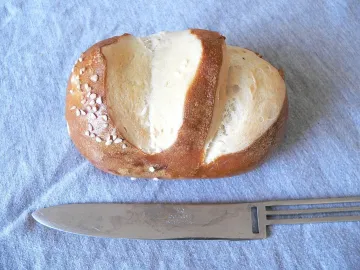 Разрезанная щелочная булочка с коркой и крупной солью