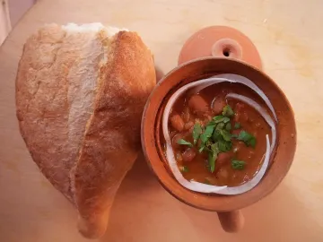 Лобио в глиняном горшочке с зеленью и луком рядом с хлебом