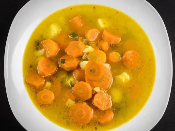 Морковный суп с кружками моркови и картофелем в белой тарелке
