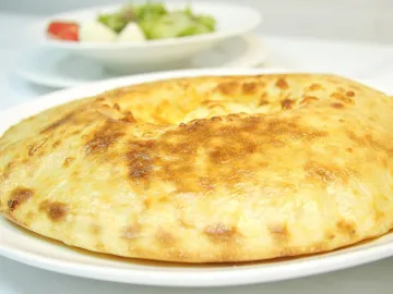 Осетинский пирог с сыром и картофелем на белой тарелке