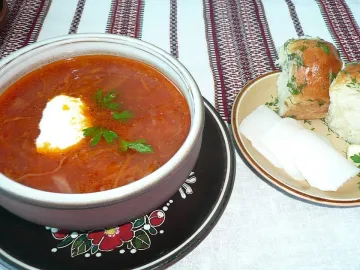 Пампушки с чесноком и укропом рядом с тарелкой борща