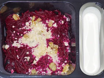 Салат из тёртой свёклы с изюмом и измельчёнными орехами в чёрном контейнере