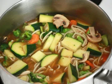 Кастрюля супа с лапшой удон, кабачком, брокколи и шампиньонами