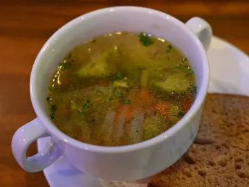 Прозрачный овощной суп с брокколи и морковью в белой чашке с хлебом