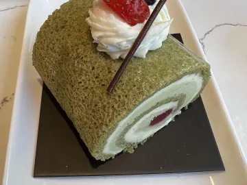 Кусок зелёного рулета с матчей, сливками и клубникой