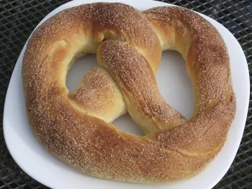 Сдобный крендель, посыпанный сахаром с корицей, на белой тарелке