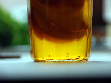 Золотистая настойка с дольками яблока и нитями шафрана в стакане