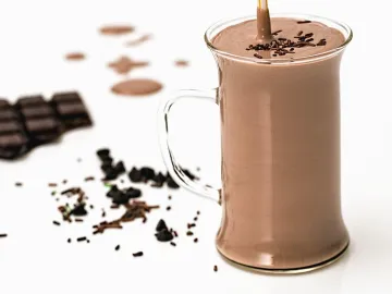 Высокая стеклянная кружка с коричневым шоколадным напитком, рядом плитка шоколада и шоколадная крошка