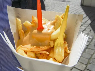 Картофель фри в бумажном кульке, политый оранжевым соусом