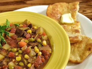 Суп с говядиной, кукурузой, горошком и томатами в жёлтой тарелке