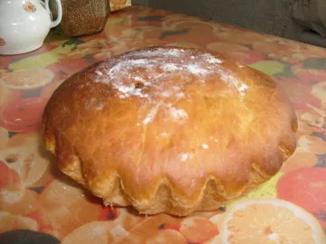 Круглая сдобная паска с золотистой корочкой и мучной присыпкой на столе