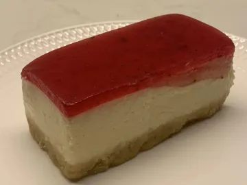 Кусок пирожного с основой из печенья, сливочным слоем и клубничным желе