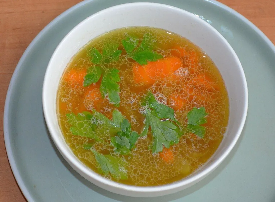 Белая миска с прозрачным бульоном, морковью и петрушкой