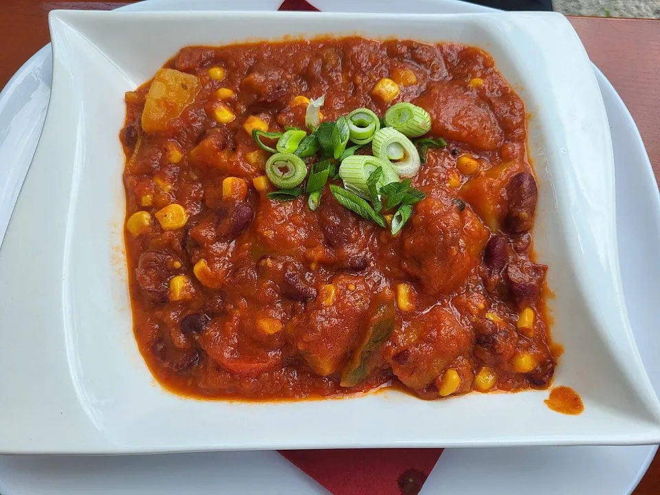 Чили с красной фасолью, кукурузой и зелёным луком в белой тарелке