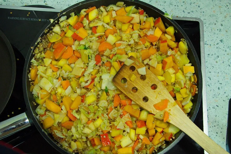 Гречка с капустой, тыквой и морковью на сковороде с лопаткой