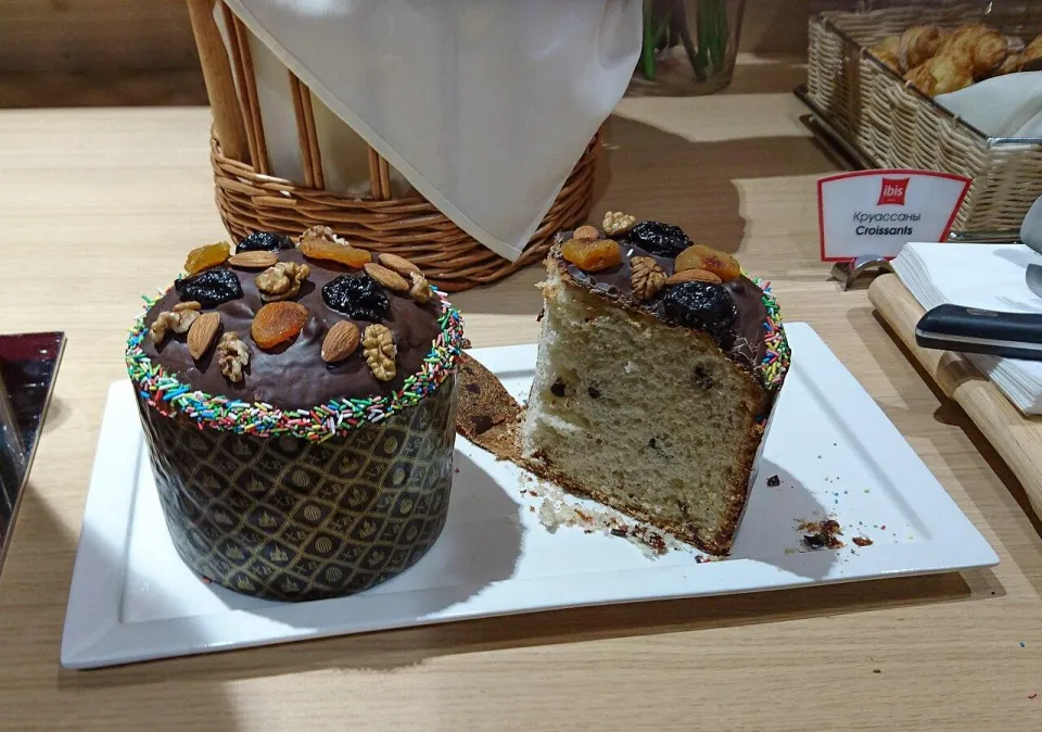 Пасхальный кулич с шоколадной глазурью, орехами и сухофруктами, рядом отрезанный кусок