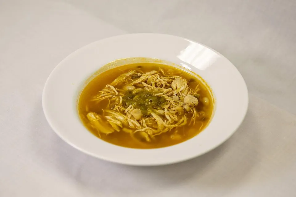 Куриный суп с белой фасолью и зеленью в белой тарелке