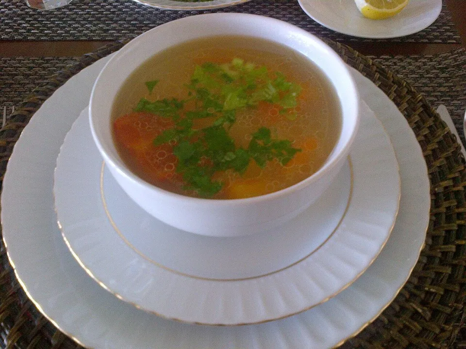 Прозрачный куриный суп с морковью и зеленью в белой миске