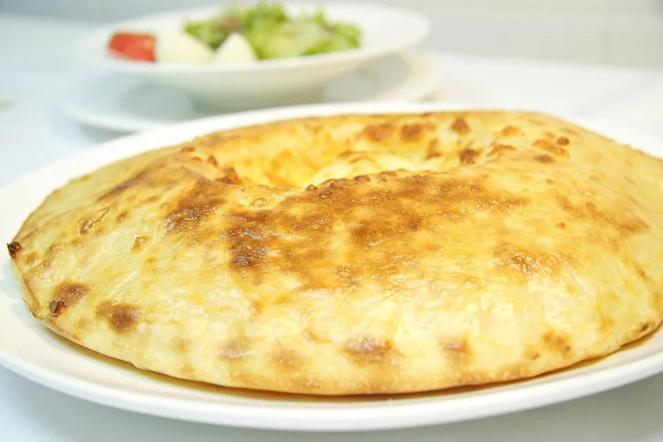 Осетинский пирог с сыром и картофелем на белой тарелке