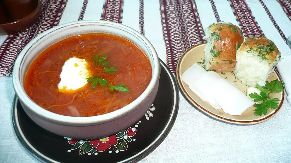 Пампушки с чесноком и укропом рядом с тарелкой борща