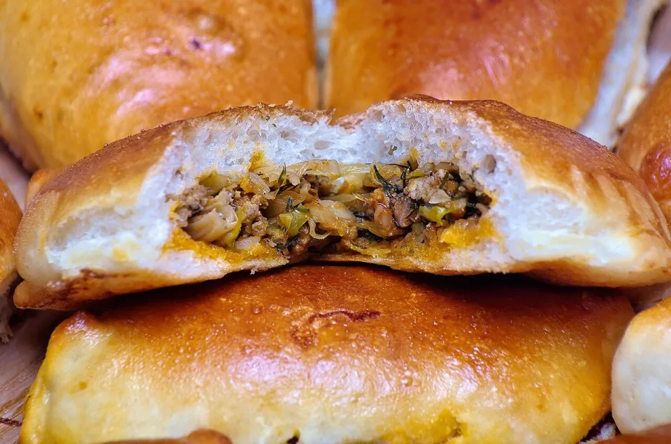 Разломленный румяный пирожок с мясом и капустой
