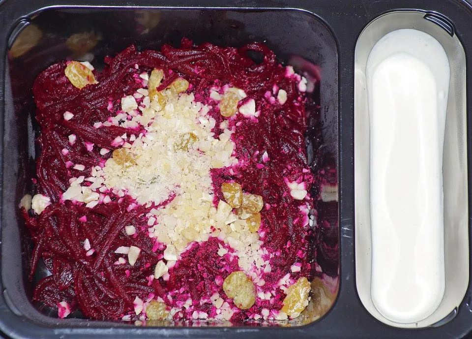 Салат из тёртой свёклы с изюмом и измельчёнными орехами в чёрном контейнере