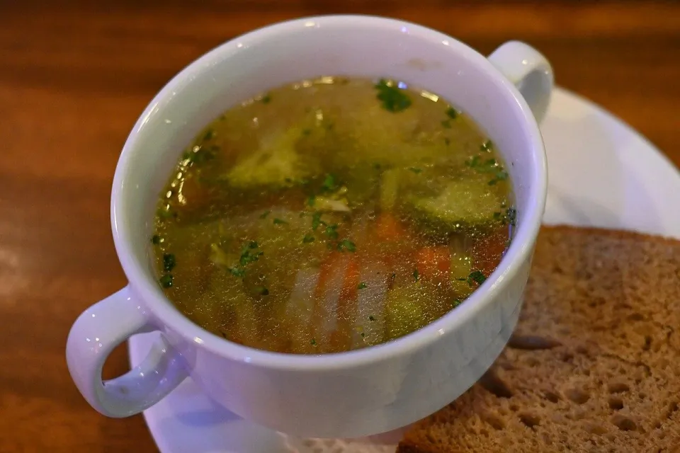Прозрачный овощной суп с брокколи и морковью в белой чашке с хлебом