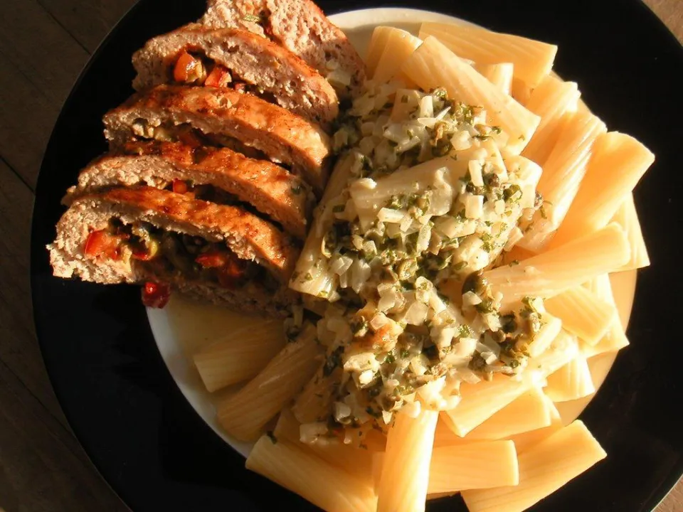 Нарезанный рулет из куриного фарша с перцем и макароны с соусом на тарелке