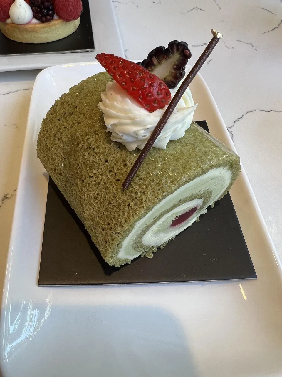 Кусок зелёного рулета с матчей, сливками и клубникой