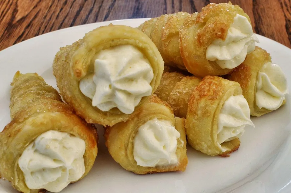 Слоёные трубочки с белым кремом и сахарной корочкой на тарелке