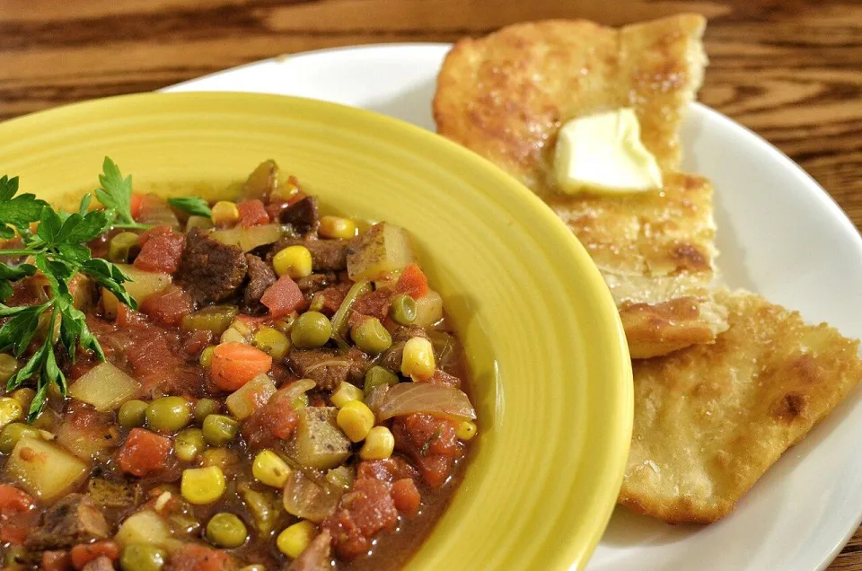Суп с говядиной, кукурузой, горошком и томатами в жёлтой тарелке
