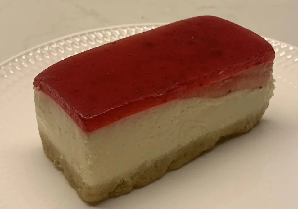 Кусок пирожного с основой из печенья, сливочным слоем и клубничным желе